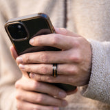 Man wearing "The Blaze" tungsten ring in black and rose gold holding a black iPhone
