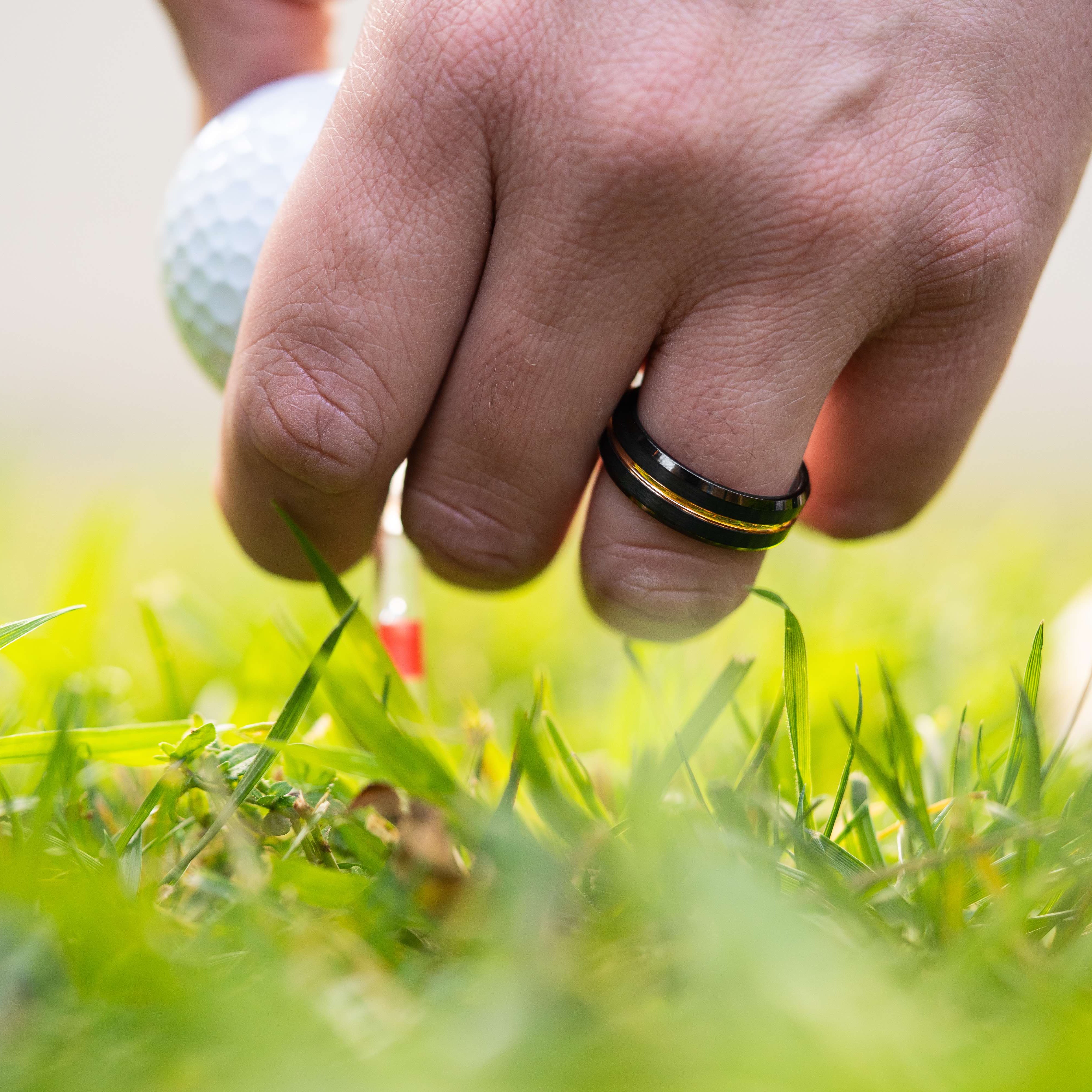 Man wearing "The Blaze" tungsten ring in black and rose gold putting a golf tee into the green