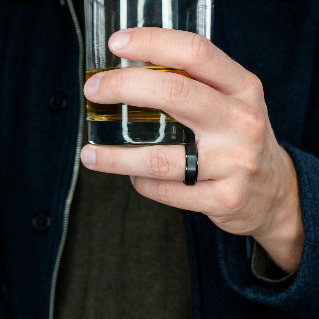 Man wearing "The Gotham" black tungsten ring with a brushed finish holding a rocks glass with whiskey in it