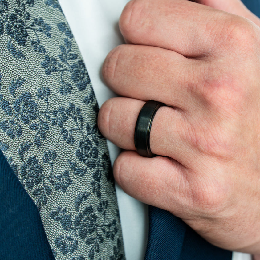Man wearing "The Gotham" black tungsten ring with a brushed finish holding the lapel of his blue suit jacket