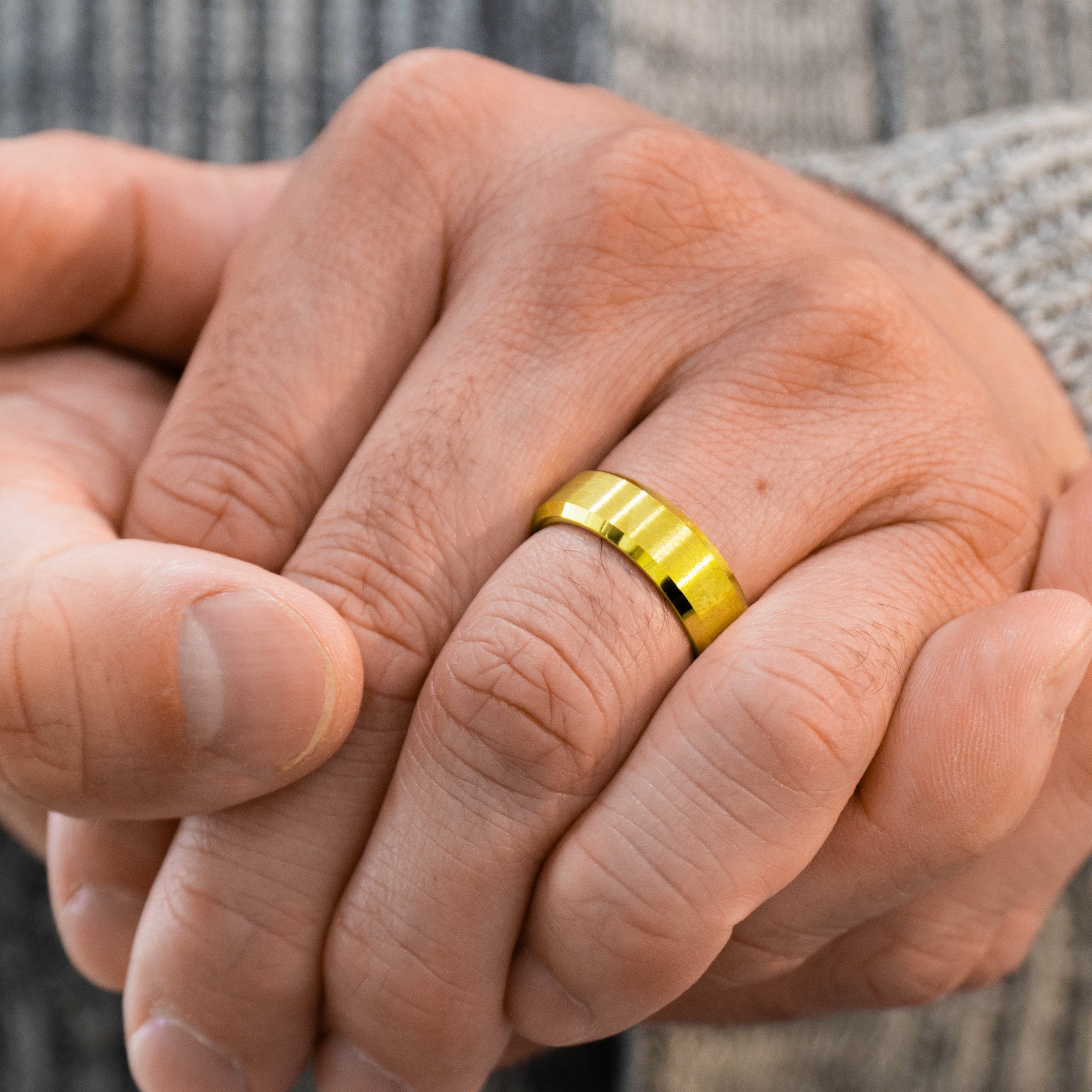 Closeup of a man wearing "The Vintage" tungsten ring in brushed gold wearing a grey sweater with his hands crossed in front of him