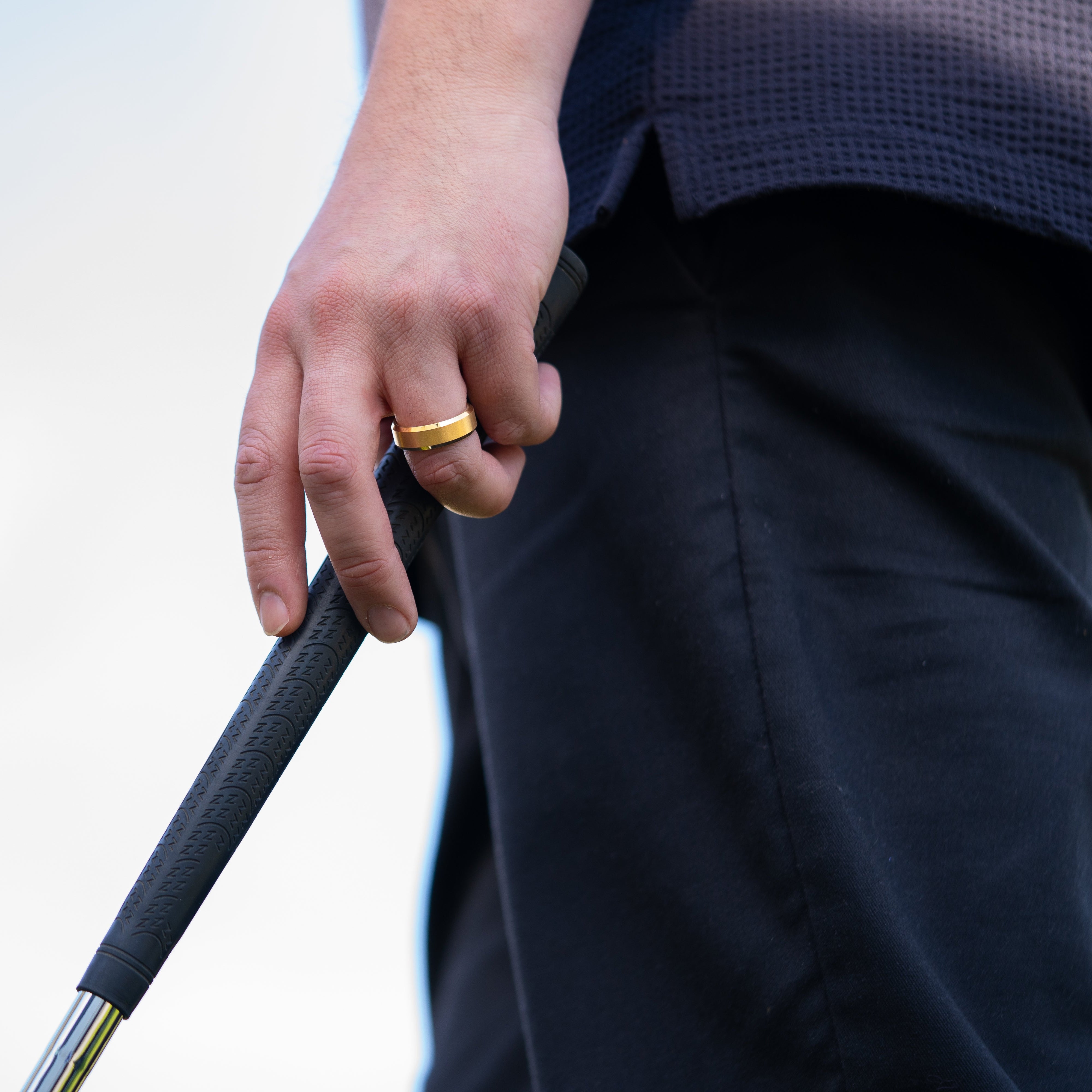 Man wearing "The Vintage" tungsten ring in brushed gold wearing blue pants and a blue top holding a golf club outside